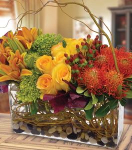 yellow roses orange lilies red pincushion protea in rectangular glass vase