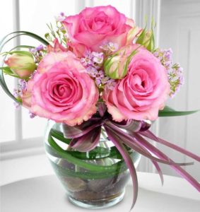 Three large open pink roses with greens in a vase