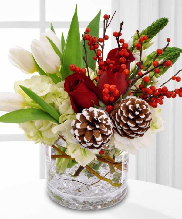 White tulips red roses berries and pine cones in glass vase