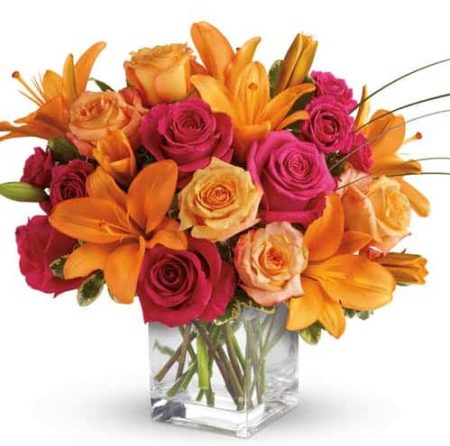 vibrant mixture of opulent orange and zesty pink flowers casually arranged in a clear glass cube container.