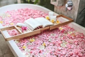 Bath full of pink flower petals with candles and open book